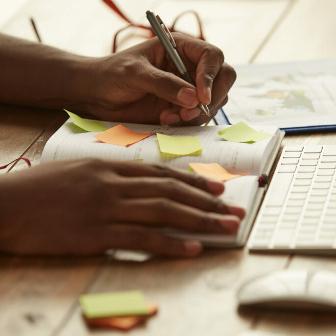 Cropped photo of afro american businessman making some notes while working remotely at home. Male hands taking notes. Freelance Cropped photo of afro american businessman making some notes while working remotely at home. Male hands taking notes. Freelance. Home office workplace